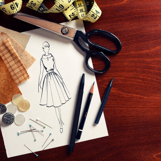Scissors, fashion drawing, pencils and measuring tape on a dark wooden desk top